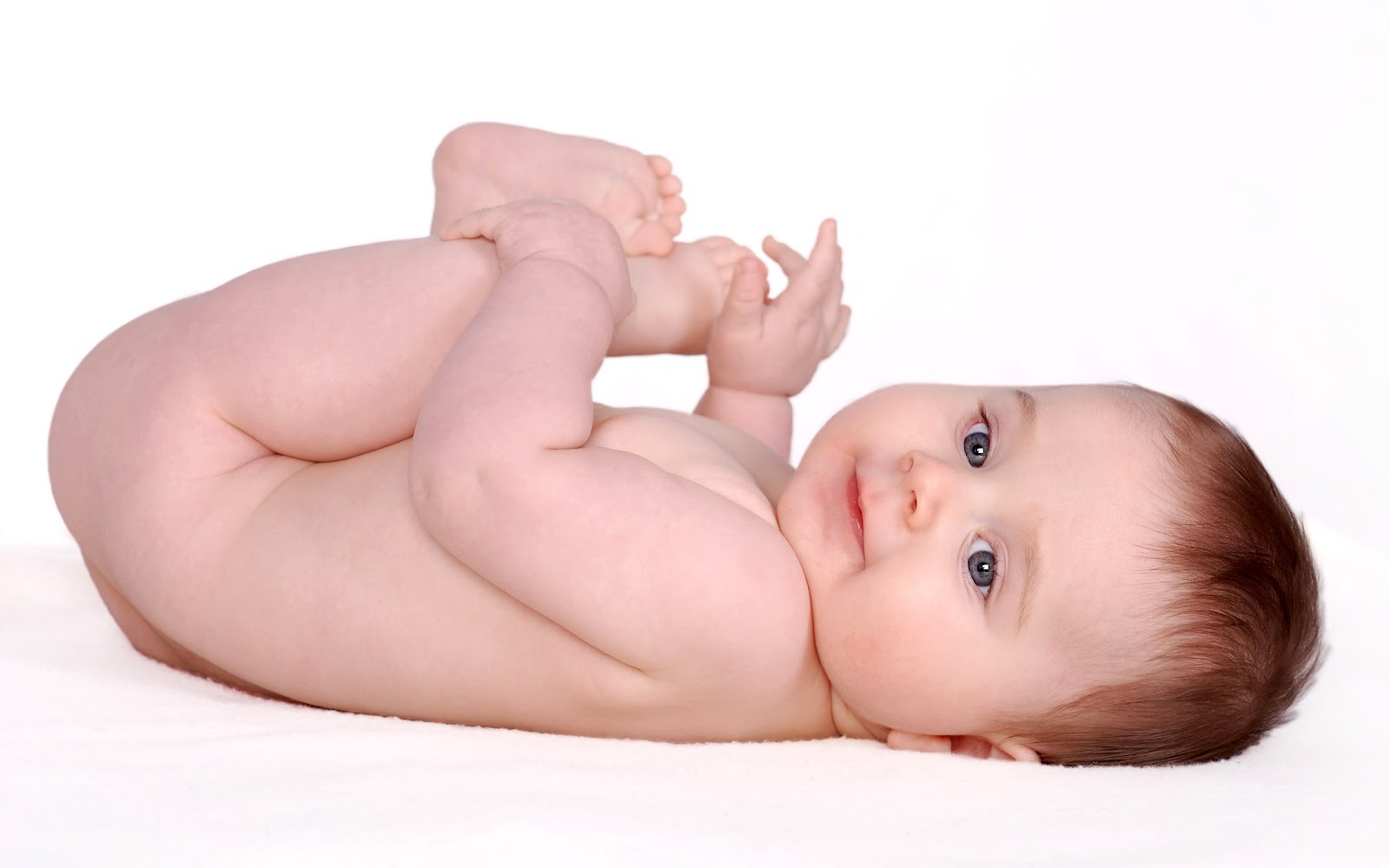 Soft duotone photograph of a baby lying on a white blanket, rendered in warm cream and pale lavender tones, gentle and tender mood